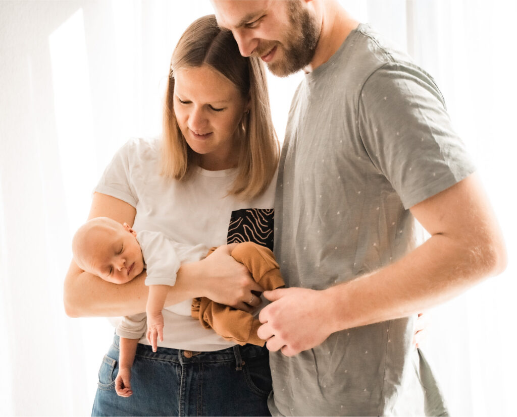 Fotot Eltern betrachten Baby auf dem Arm, © A-Line-Photography Aylin Trautter