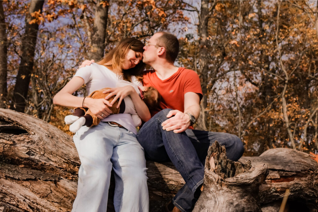 Foto glückliche junge eltern auf Baumstumpf mit Baby auf dem Arm, © A-Line-Photography Aylin Trautter
